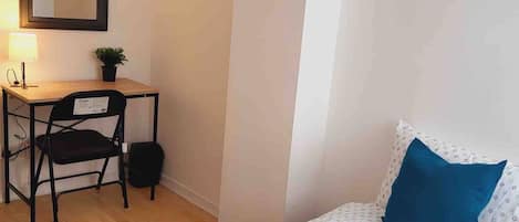A bedroom with a bed, a desk, a chair, and a small potted plant.