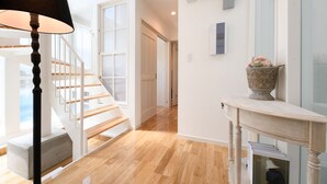 A spacious hallway with wooden flooring, a staircase, and a white console table with a vase. - Wakoso Harmonious Light South (Hakone)