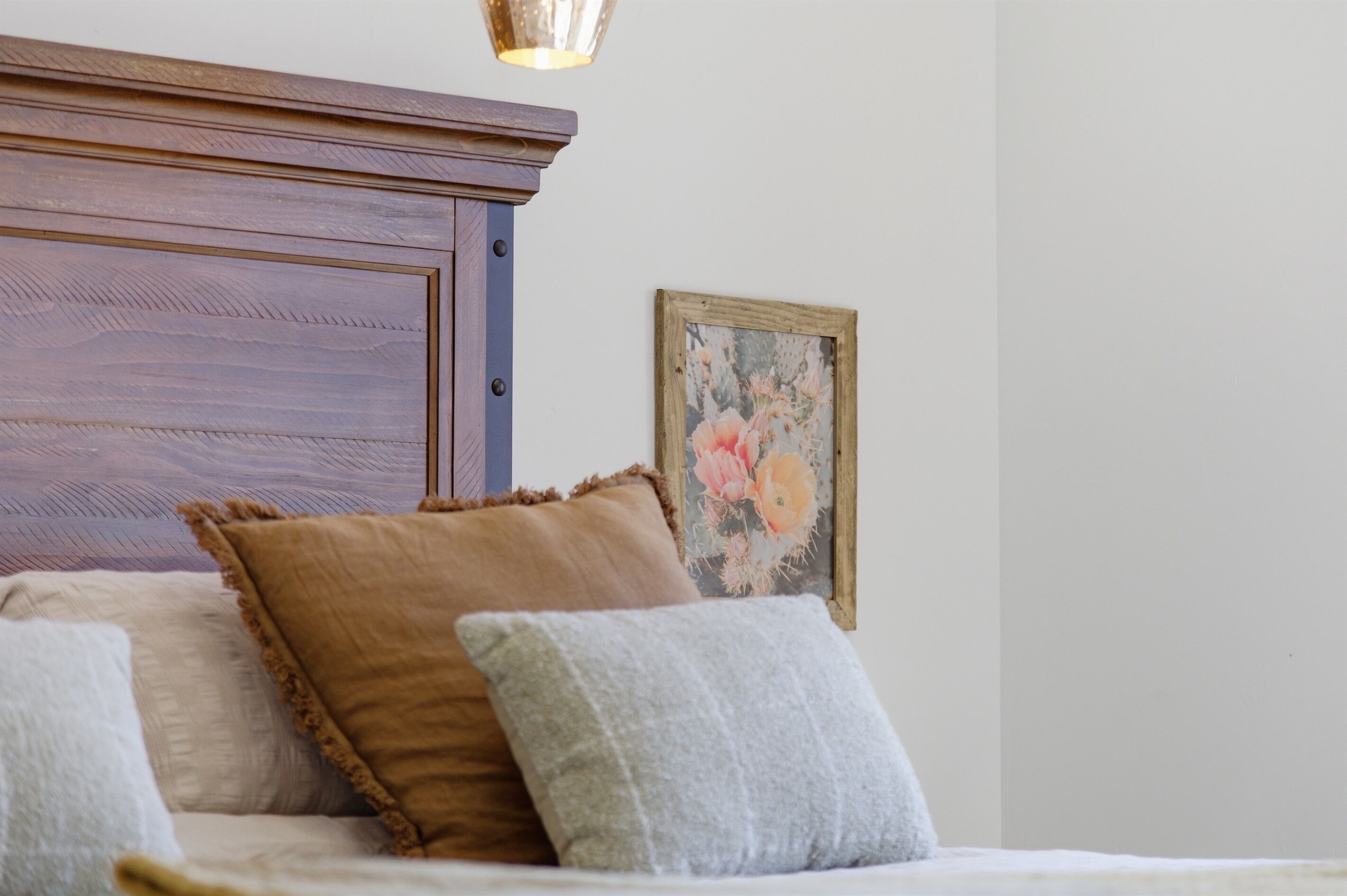 A bed with a wooden headboard, two pillows, and a floral picture on the wall.