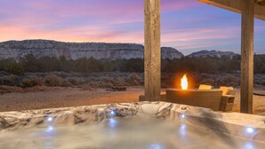 Ein Whirlpool mit Feuerstelle, eine hölzerne Pergola und Blick auf felsige Berge.