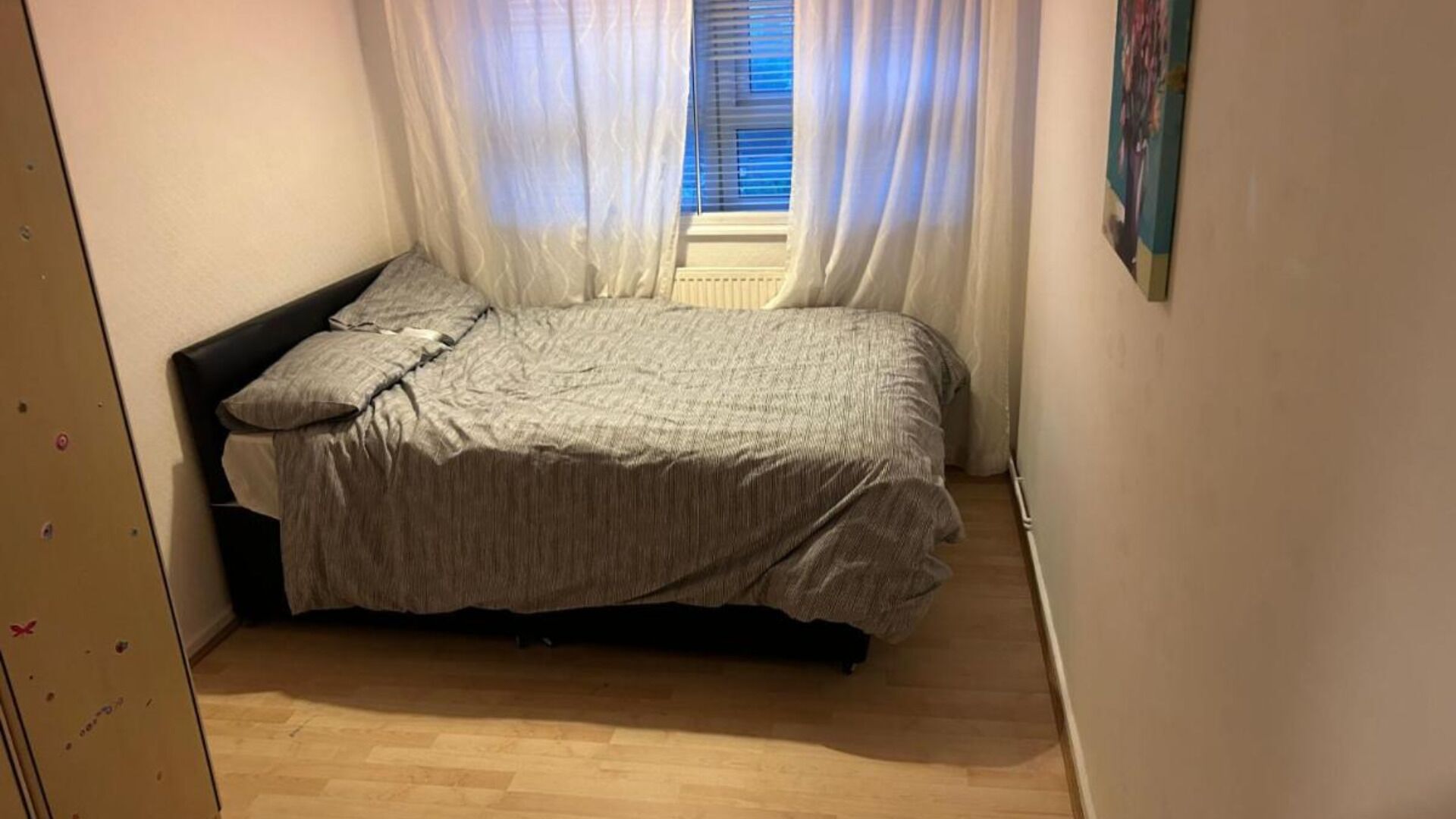 A small bedroom with a bed, a window with blinds, and a door.