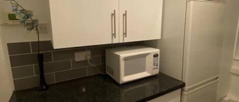 Eine Küche mit weißen Schränken, einer weißen Mikrowelle und einem weißen Kühlschrank.