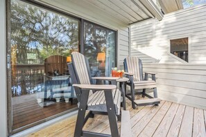 Relax in a serene outdoor space with a view of the surrounding trees, featuring a wooden deck with Adirondack chairs and a small table.