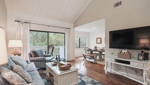 Un salón amplio con televisor grande, asientos cómodos, zona de comedor y vistas al exterior.