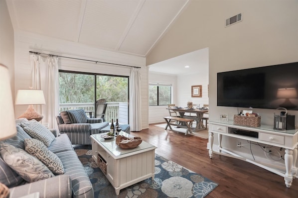 A spacious living room with a large TV, comfortable seating, a dining area, and a view of the outdoors.