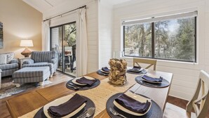 Un comedor con una mesa dispuesta para cuatro personas, un sofá y vistas a árboles por la ventana.