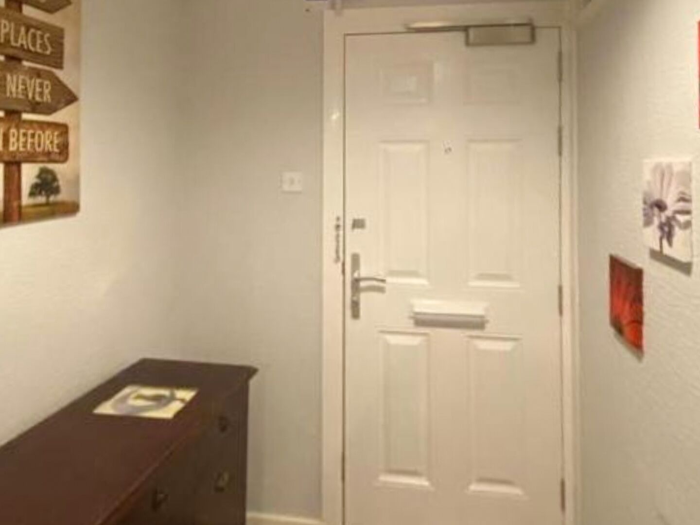 A hallway with a white door, a wooden cabinet, and a wall with signs.