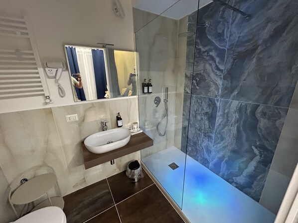 A modern bathroom with a glass-enclosed shower, a white sink, and a mirror above it. - Vomero Suite and deluxe room (Naples)