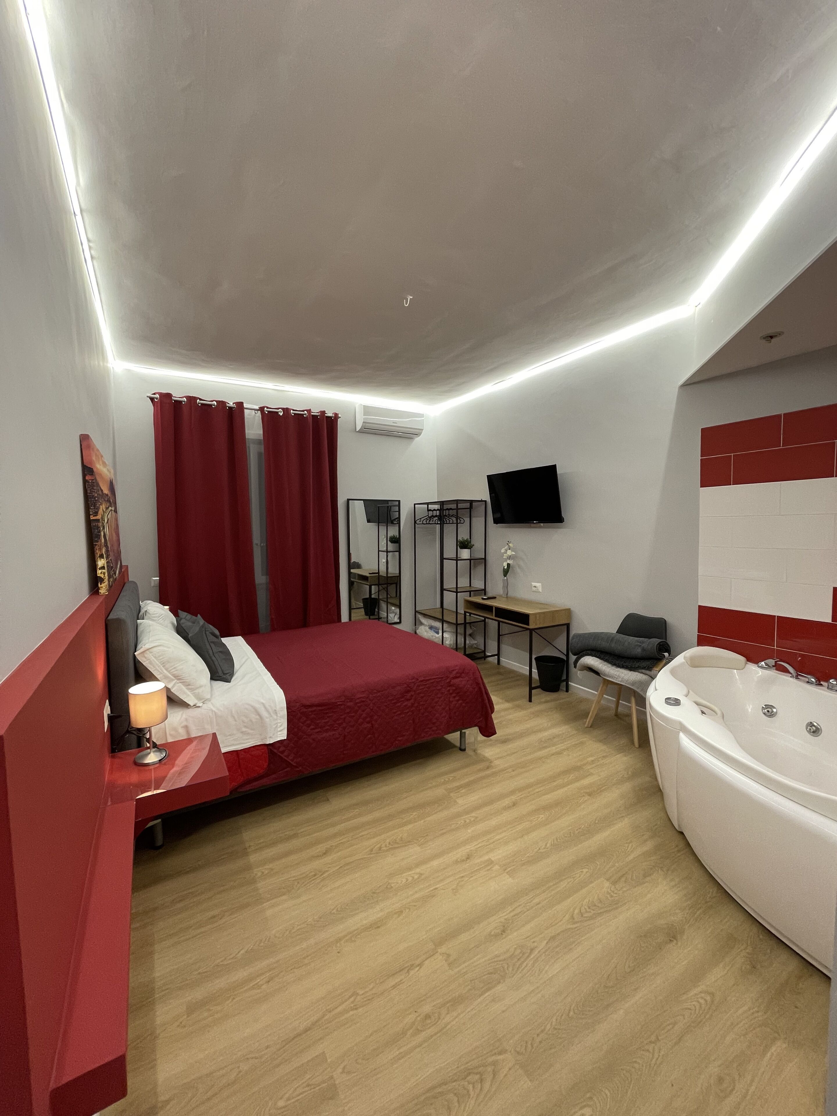 A modern bedroom with a bed, a desk, a chair, a TV, and a bathtub.