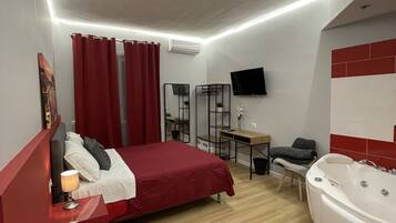 A modern bedroom with a bed, a desk, a chair, a TV, and a bathtub.
