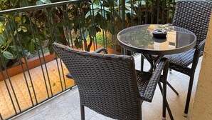 A balcony with wicker chairs and a glass table, surrounded by lush green plants. - Vomero Suite and deluxe room (Naples)