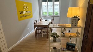 A room with a dining table, chairs, a lamp, a shelf with items, and a window with blinds. - Vomero Suite and deluxe room (Naples)
