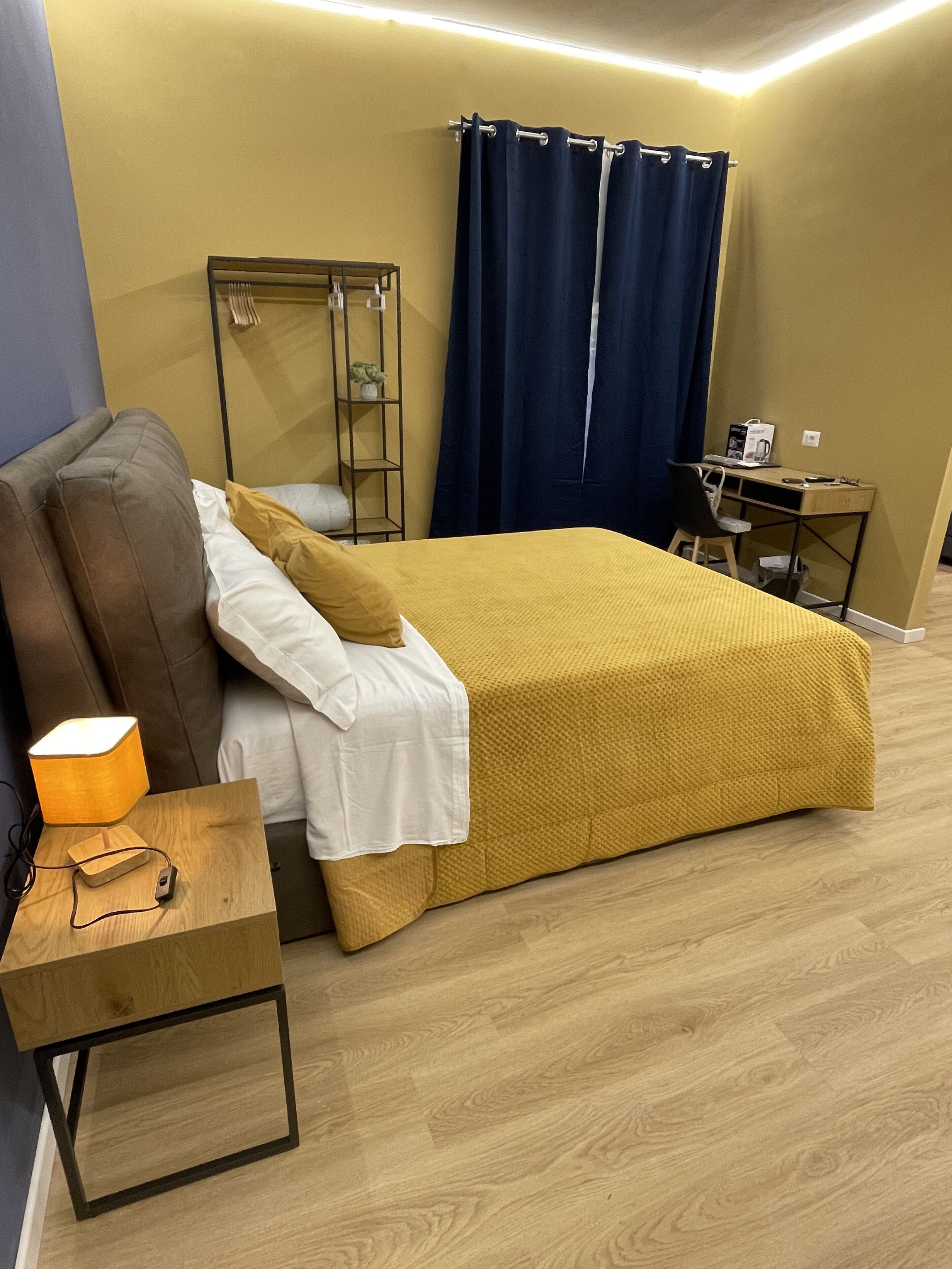A bedroom with a bed, bedside table, lamp, and a desk with a chair.