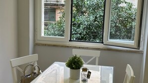 A dining area with a white table and chairs, a small potted plant, and a bottle with a label. - Vomero Suite and deluxe room (Naples)