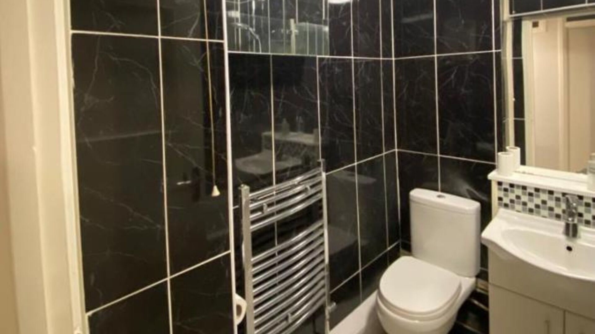 Une salle de bain avec des carreaux de marbre noir, des toilettes blanches, un lavabo blanc et un miroir au-dessus du lavabo.