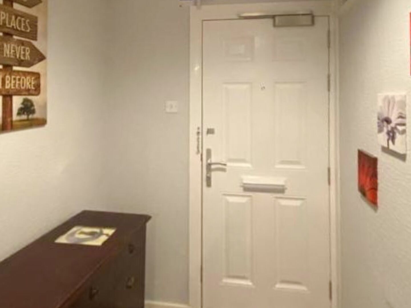 A hallway with a white door, a dark wooden cabinet, and a wall with signs.