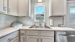 A modern kitchen with white cabinets, a stainless steel sink, and a window above the sink.