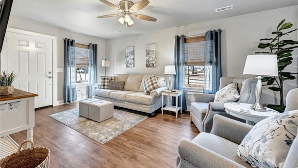 A living room with a sofa, armchairs, a coffee table, and a ceiling fan.