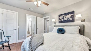 A bedroom with a bed, a ceiling fan, a world map artwork, and a lamp on the wall.