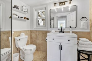 Ein Badezimmer mit Toilette, Waschbecken, Spiegel und Ablagen für Toilettenartikel.