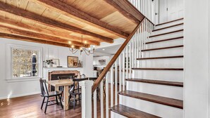 Une cuisine spacieuse avec un plafond en bois et des murs blancs, un coin repas avec une table et des chaises, et un escalier avec des marches en bois.