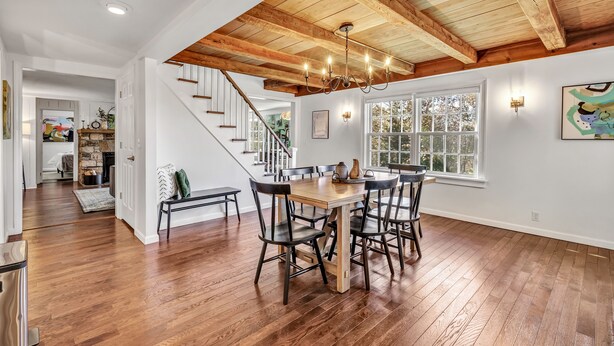 Un vaste espace dédié à la salle à manger, avec une table et des chaises en bois, un lustre et un escalier menant à un autre niveau.