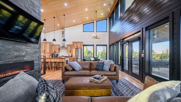 Una sala de estar moderna con chimenea, sofá de cuero y grandes ventanales que ofrecen vistas al exterior.