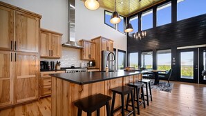 Una cocina moderna con armarios de madera, una isla central con taburetes, una estufa y un amplio ventanal con vistas panorámicas.