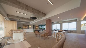 Un hall d’hôtel spacieux, doté de meubles en osier, d’un comptoir d’accueil et de grandes fenêtres offrant une vue panoramique.