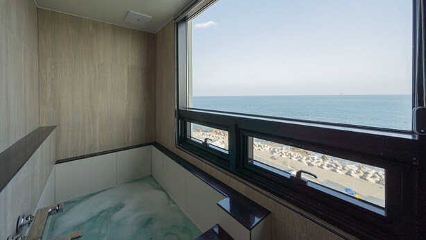Une salle de bain avec une baignoire, une fenêtre donnant sur la plage et un mur en bois.