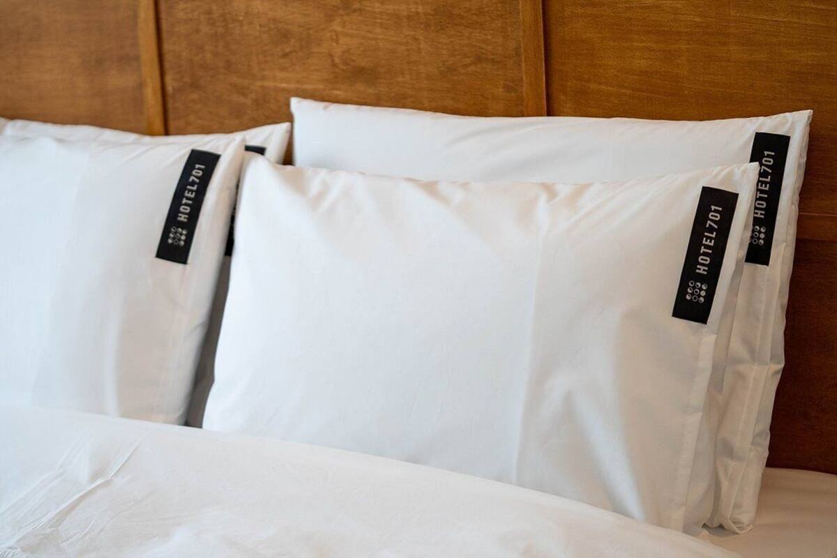 Una cama con ropa de cama y almohadas blancas, cada una con una etiqueta negra que dice "HOTEL701".
