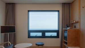 Une pièce dotée d’une grande fenêtre, d’un téléviseur à écran plat, d’une petite table, d’une chaise et d’une étagère en bois sur laquelle se trouvent un téléviseur et quelques objets.