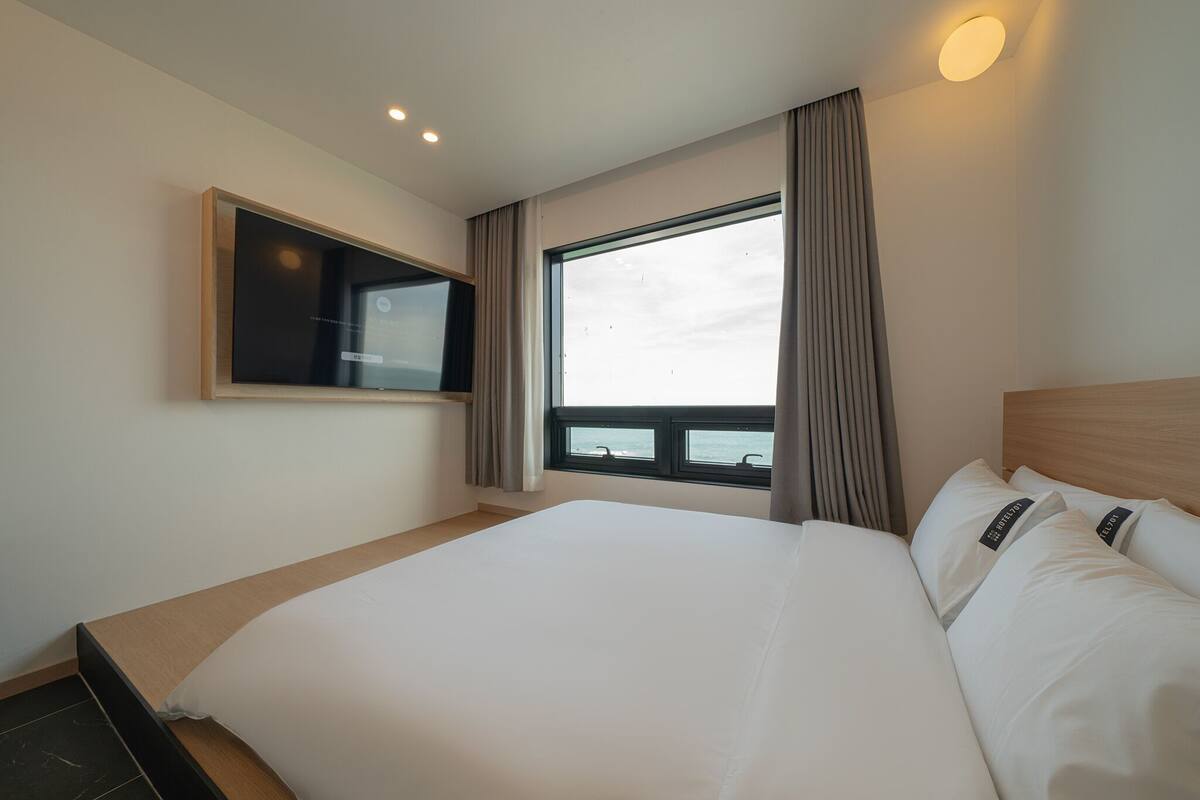 Habitación de hotel con una cama grande, un televisor montado en la pared y una ventana con cortinas.