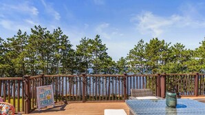 A wooden deck with outdoor furniture, a sign reading "It's Better on the Porch," and a view of trees and water.