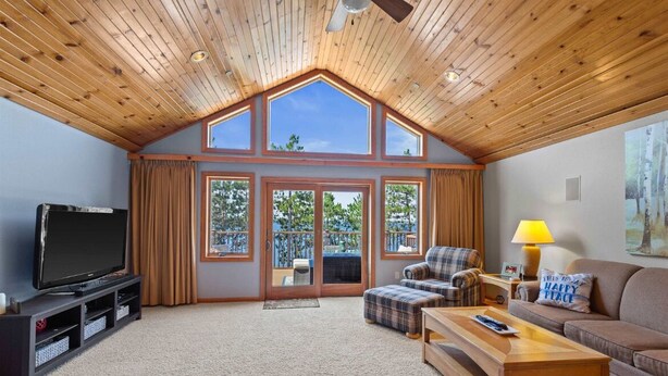 A spacious living room with a high ceiling, large windows, a flat-screen TV, a sofa, a coffee table, and a lamp.