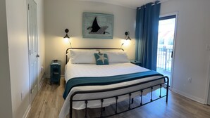 Un dormitorio con cama, mesita de noche, lámpara de pared y ventana con cortinas.