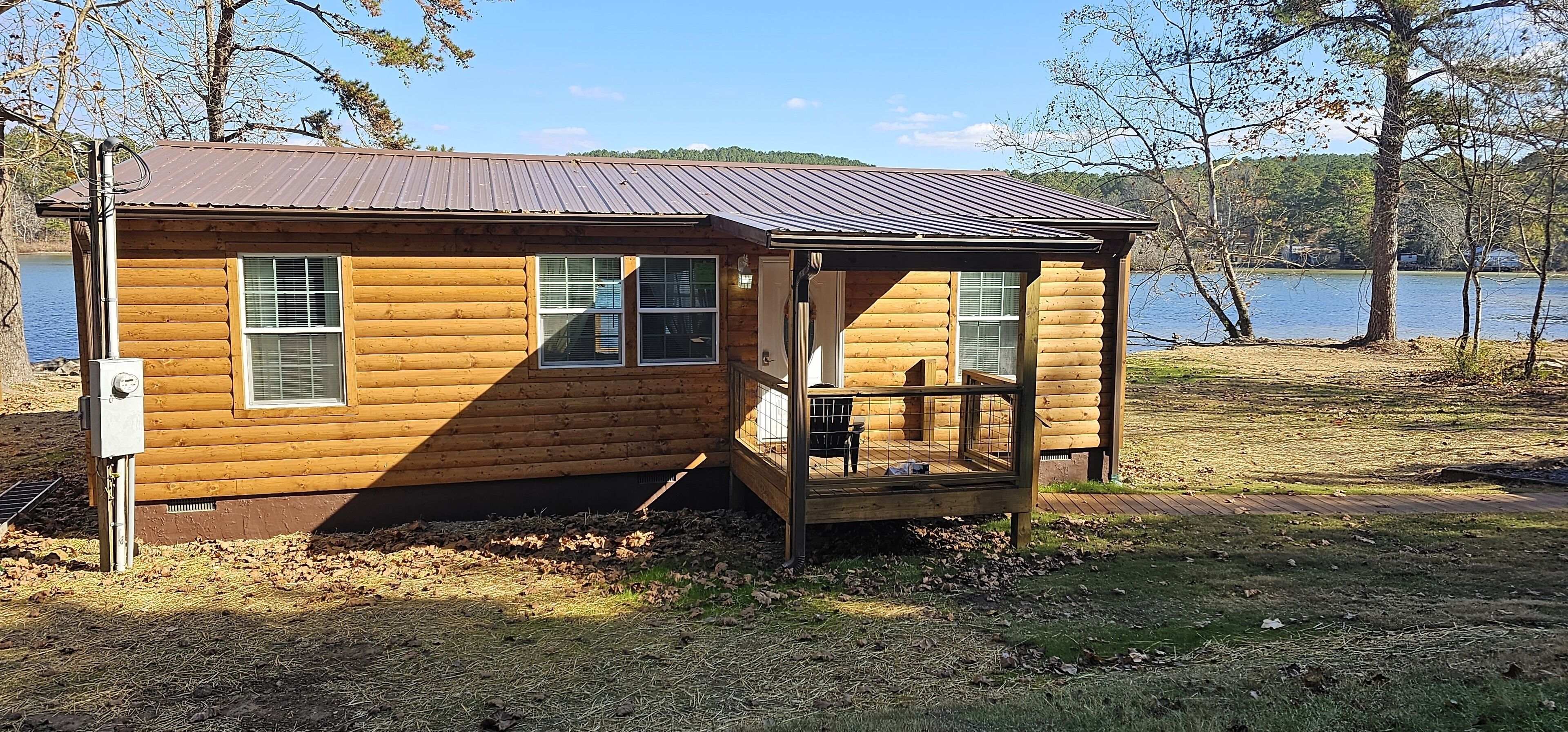 A wooden cabin with a metal roof, a porch, and a view of a lake.