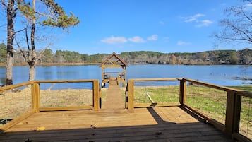 A wooden deck leading to a gazebo by a lake with a clear view of the water and surrounding trees.