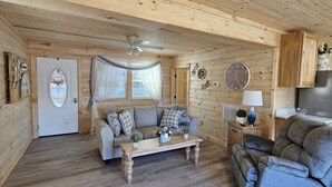 Een gezellig houten interieur met een houten plafond, een bank, een fauteuil, een eettafel en een keuken met een koelkast.