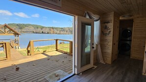 Een houten hutje met een terras dat uitkijkt over een meer, een deur naar een kamer en een kleine buitenbouw.