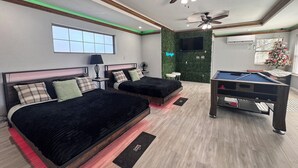 Una habitación de hotel moderna con dos camas, una mesa de billar, un ventilador de techo y una pared verde.
