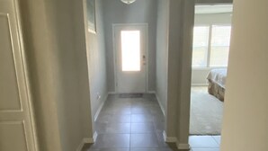 Un couloir avec une porte au fond, un luminaire au plafond et une fenêtre avec des stores.