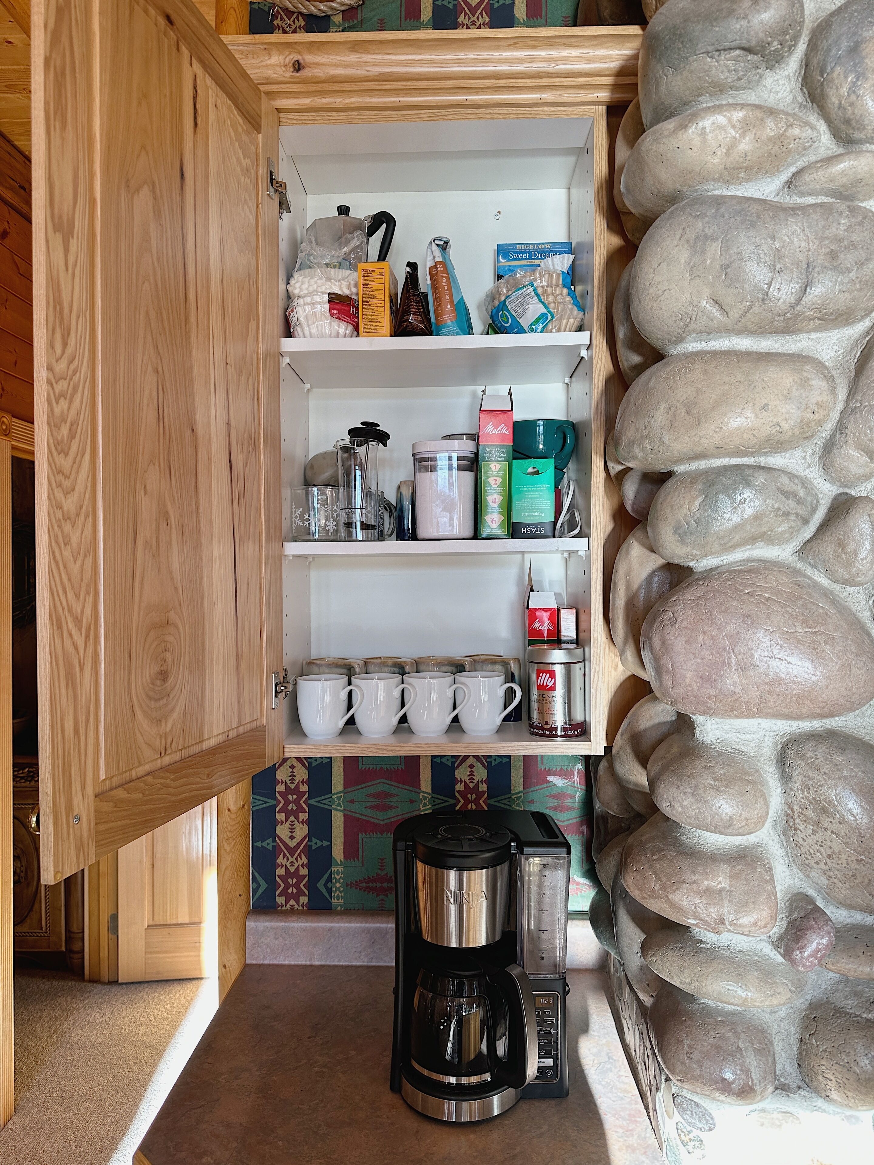 Un garde-manger avec des étagères remplies de divers produits alimentaires, une machine à café et un mur en pierre.