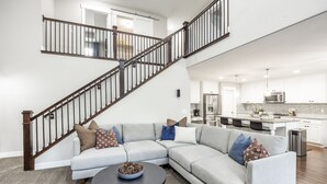 A modern living room with a grey sectional sofa, a round coffee table, and a staircase with dark railings leading to an upper level.