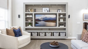 Una sala de estar moderna con un televisor de pantalla plana grande montado en una pared gris, rodeada de estanterías y cajas de almacenamiento.