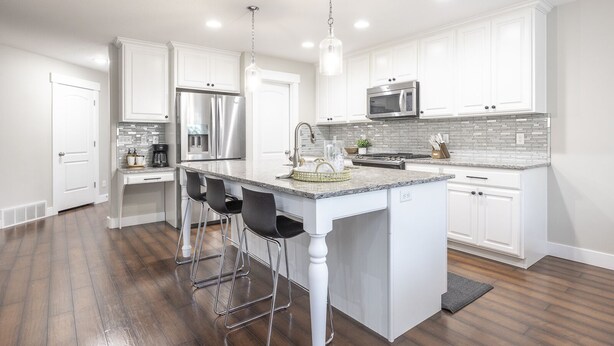 Una cocina moderna con armarios blancos, electrodomésticos de acero inoxidable, encimera de granito y una isla central con taburetes de bar.