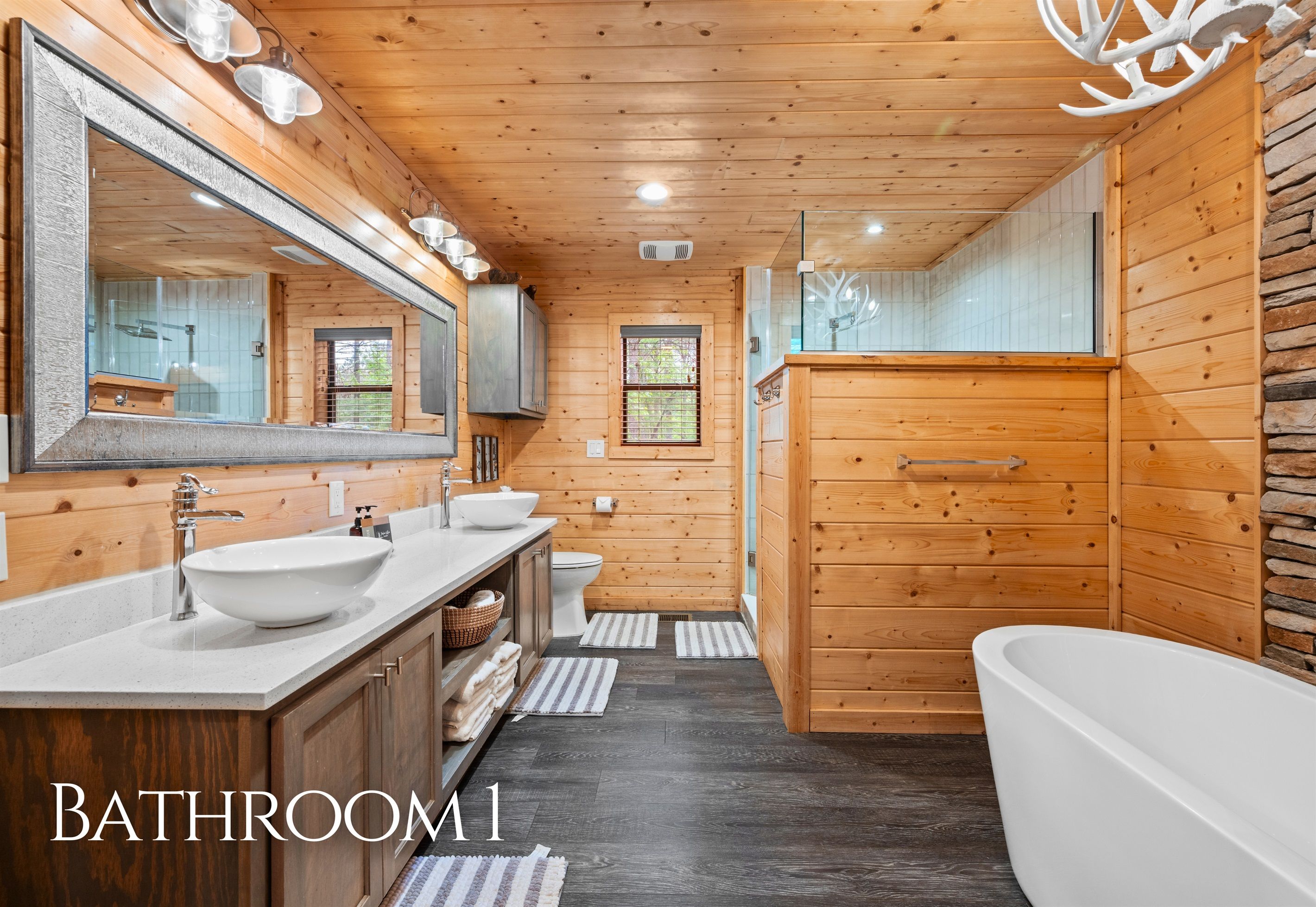 A wooden-paneled bathroom with two sinks, a toilet, and a bathtub.