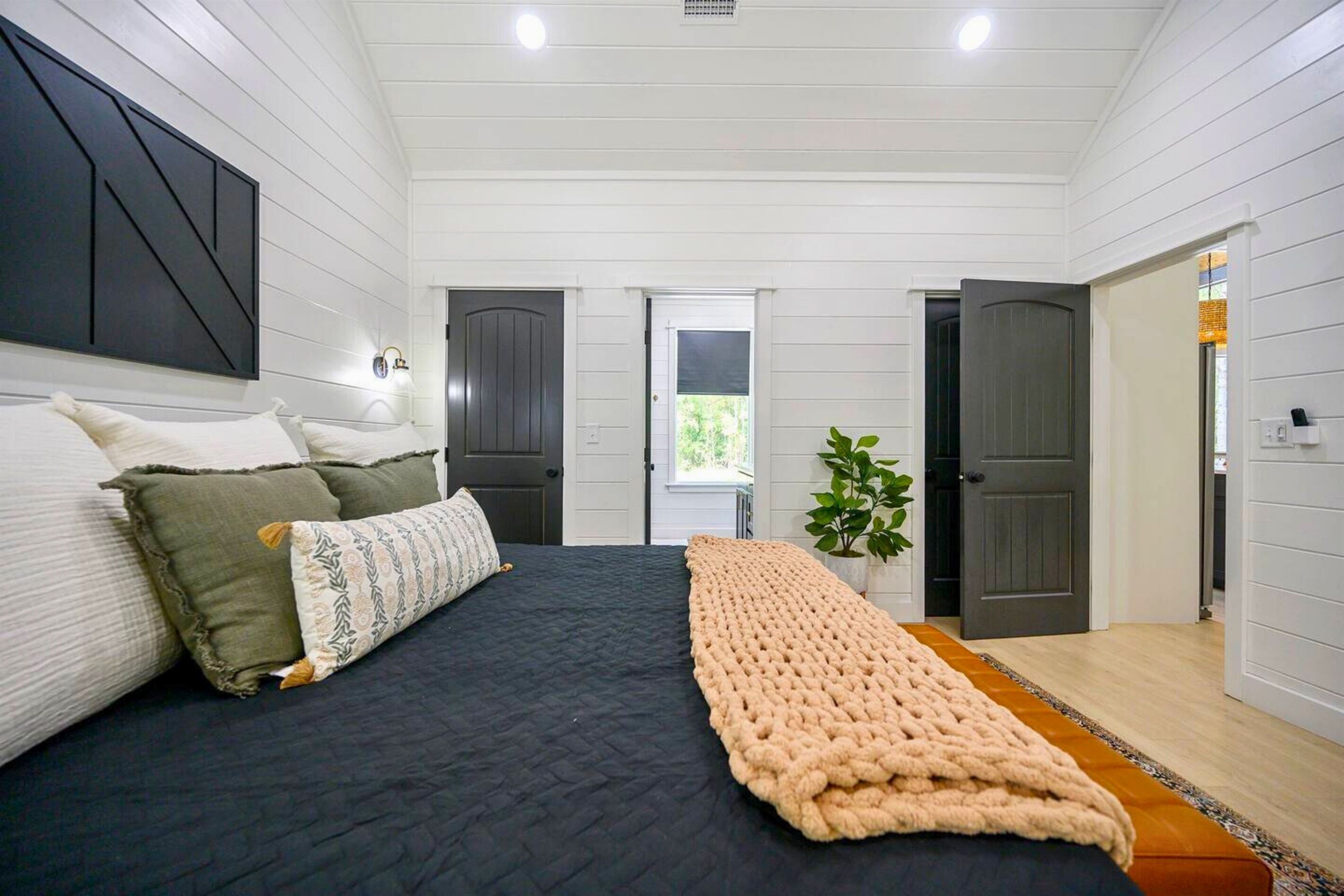 A bedroom with a large bed, a dark headboard, and a beige throw blanket.
