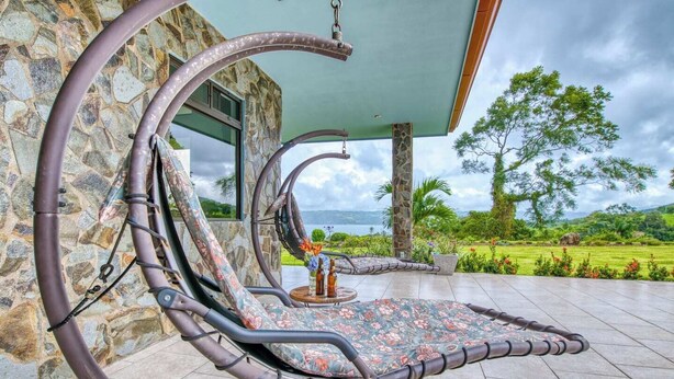 A stone building with a curved roof and a patio area with a hanging chair and a small table with bottles. - Stunning Lake  & Volcano Views (Tronadora)