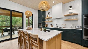 Une cuisine moderne dotée d’un grand îlot central, de meubles de rangement aux couleurs sombres et de chaises en bois.